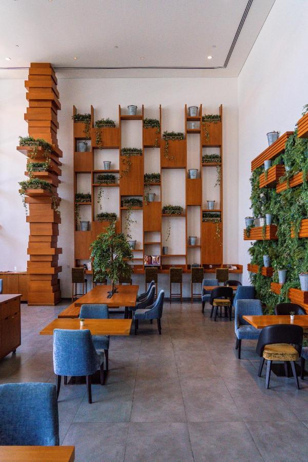 Canal Central Hotel Business Bay Dubai Exterior photo The photo shows a modern café or restaurant interior. There is a striking wooden wall featuring a series of shelves filled with potted plants, creating a lush green backdrop. On one side, there is a tall, vertical wooden structure that adds architect