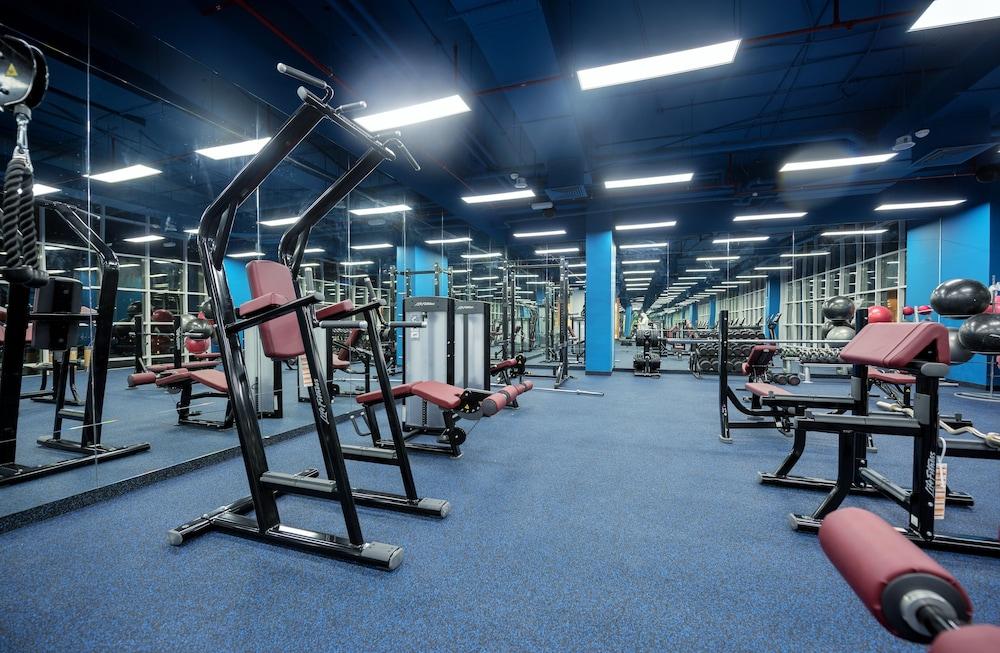 Canal Central Hotel Business Bay Dubai Exterior photo The photo shows a gym interior with various exercise equipment. There are machines designed for strength training, including a multi-station machine and benches. The floors are covered with blue carpet, and there are large mirrors on the walls, refle