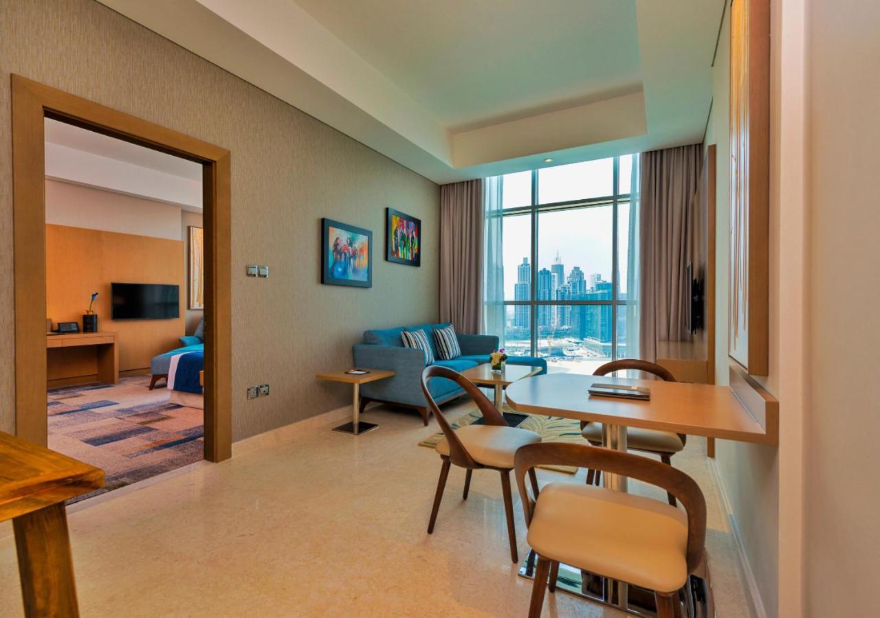 Canal Central Hotel Business Bay Dubai Exterior photo The photo shows a modern interior space, likely a living area or suite. On one side, there’s a small dining table with chairs, and on the other, a comfortable couch positioned near large windows that allow natural light to fill the room. The walls ar