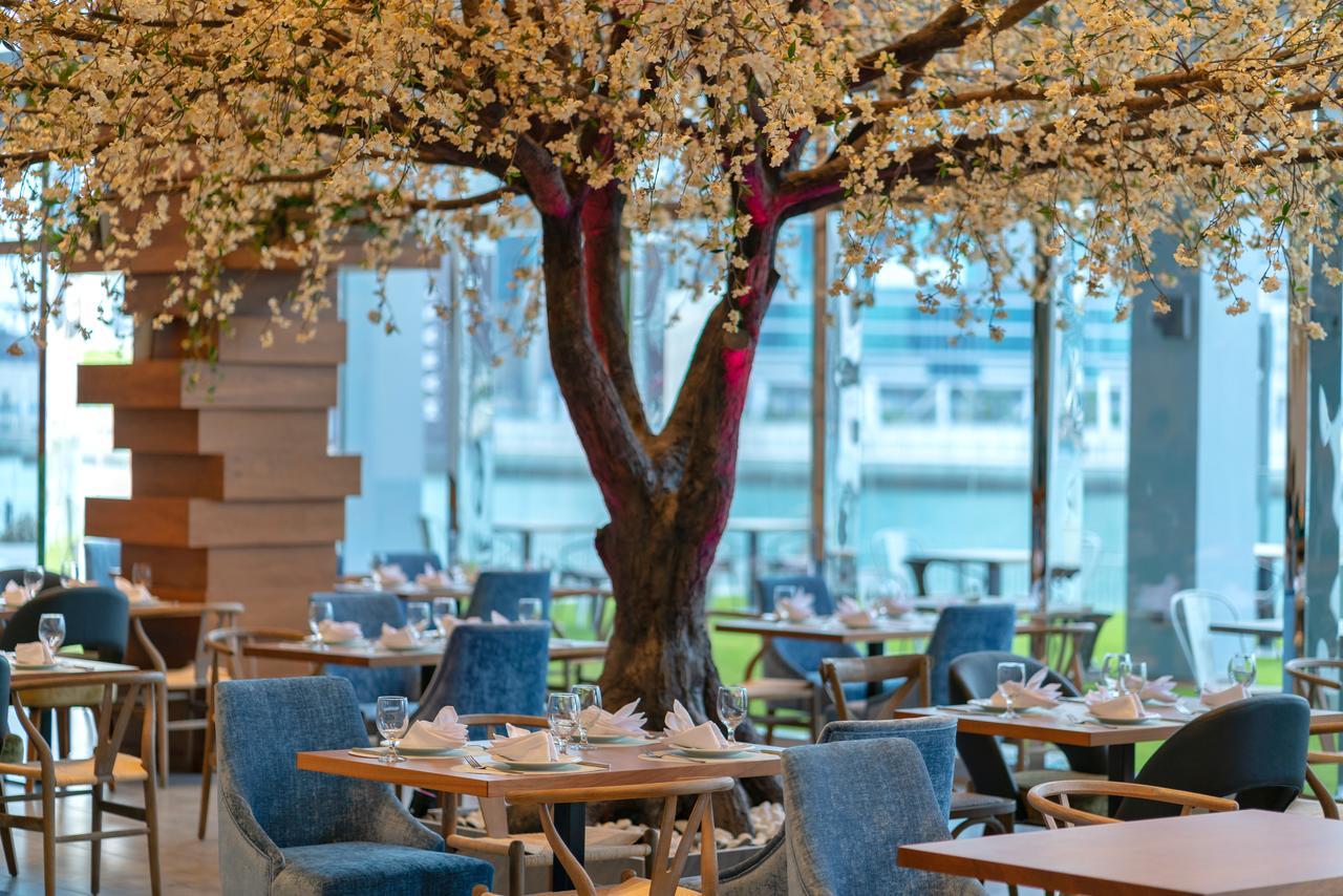 Canal Central Hotel Business Bay Dubai Exterior photo The photo depicts an elegantly designed restaurant interior featuring a large, decorative tree in the center. The tree has a thick trunk and branches adorned with delicate, white flowers, creating a charming and inviting atmosphere. Surrounding the t