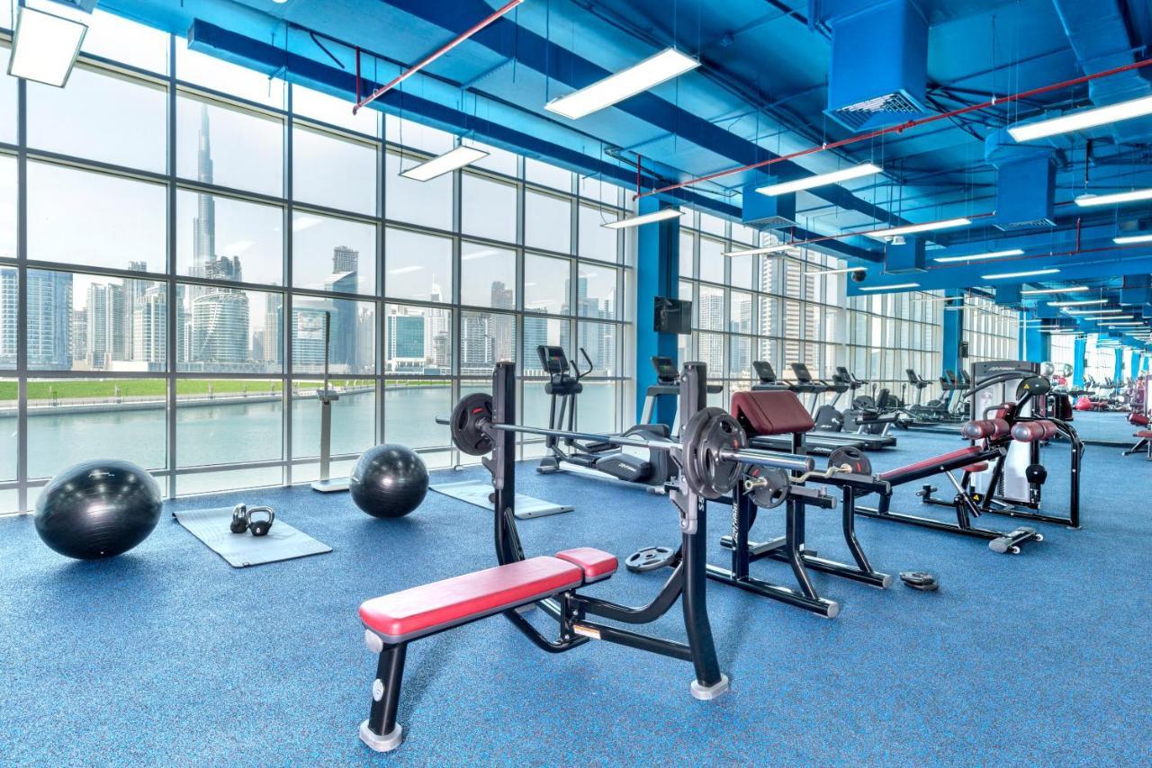 Canal Central Hotel Business Bay Dubai Exterior photo The photo shows a modern gym with a vibrant blue ceiling and walls. It features large windows that provide a view of a city skyline. Inside, there are various workout machines, including a bench press and cardio equipment. Additionally, there are exe